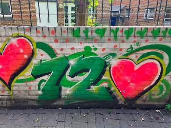Number 72 graffitied on a wall with hearts next to it